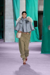 Model wearing bleached cotton capelet in gale, with a nylon jersey vest and linen trousers in khaki and milk.