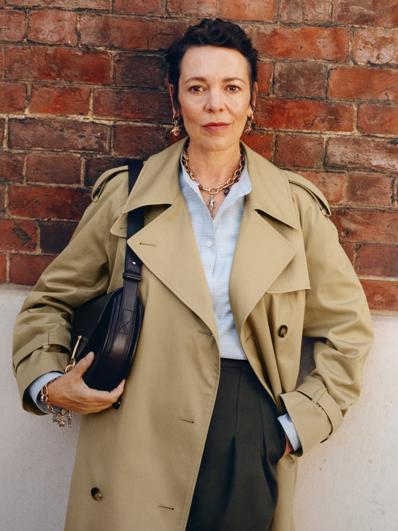 演员Olivia Colman身穿米色长款卡斯尔福德版型风衣，手持黑色小号B字型卡扣信使包
