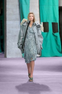 Model wearing Faux feather trim bleached cotton parka in gale and metallic paillette fringed viscose jersey dress in light blue.