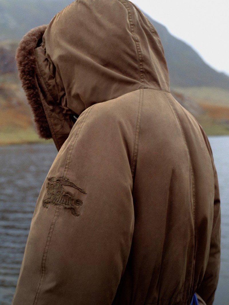 男模特身着Burberry嘎巴甸2026系列夹克，站在湖泊和森林旁 