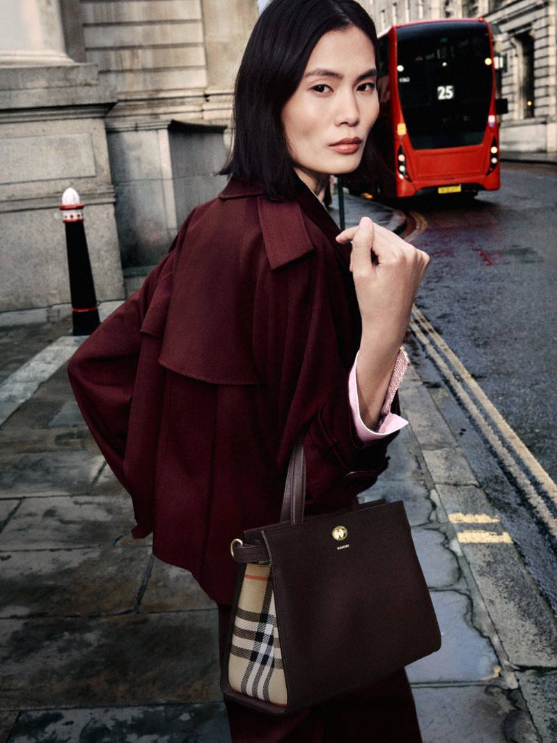 模特身穿葡萄园红短款羊毛Mayfair Trench外套，手持葡萄园红小号Cotswolds格纹托特包